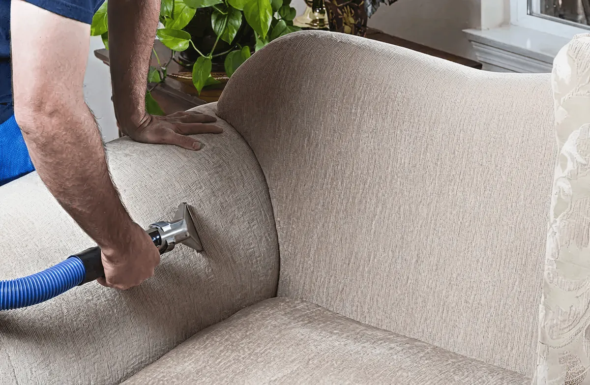 Professional upholstery cleaner deep-cleaning a fabric sofa with a handheld extraction tool and hose, Boulder, CO.